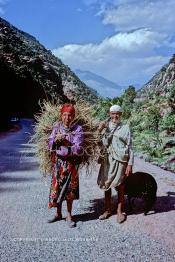 Image du Maroc Professionnelle de  Sur la route de l'Oukaimden, un couple berbère accompagné d'un petit agneau remonte la haut sur la montagne pour rejoindre son village, après une journée de labeur sur leur petit lopin plus bas sur la vallée. L'homme porte les outils du parfait agriculteur, alors que la femme transporte un peu de foin sur son dos pour sa brebis, le Dimanche 21 Décembre 1986. (Photo / Abdeljalil Bounhar)
